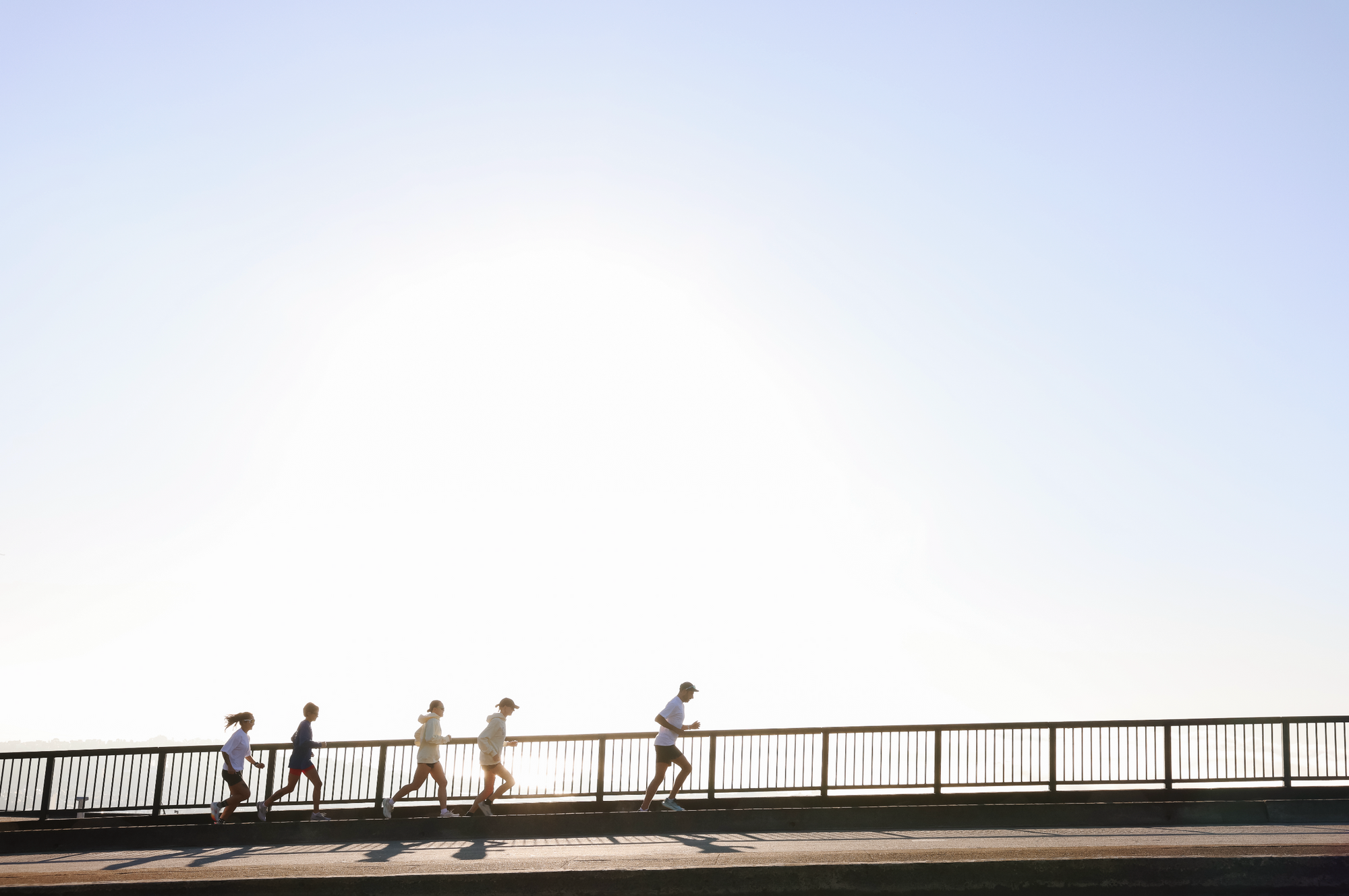 Five runners in Running Wylder apparel silhouetted against the morning sun while crossing a bridge in San Francisco