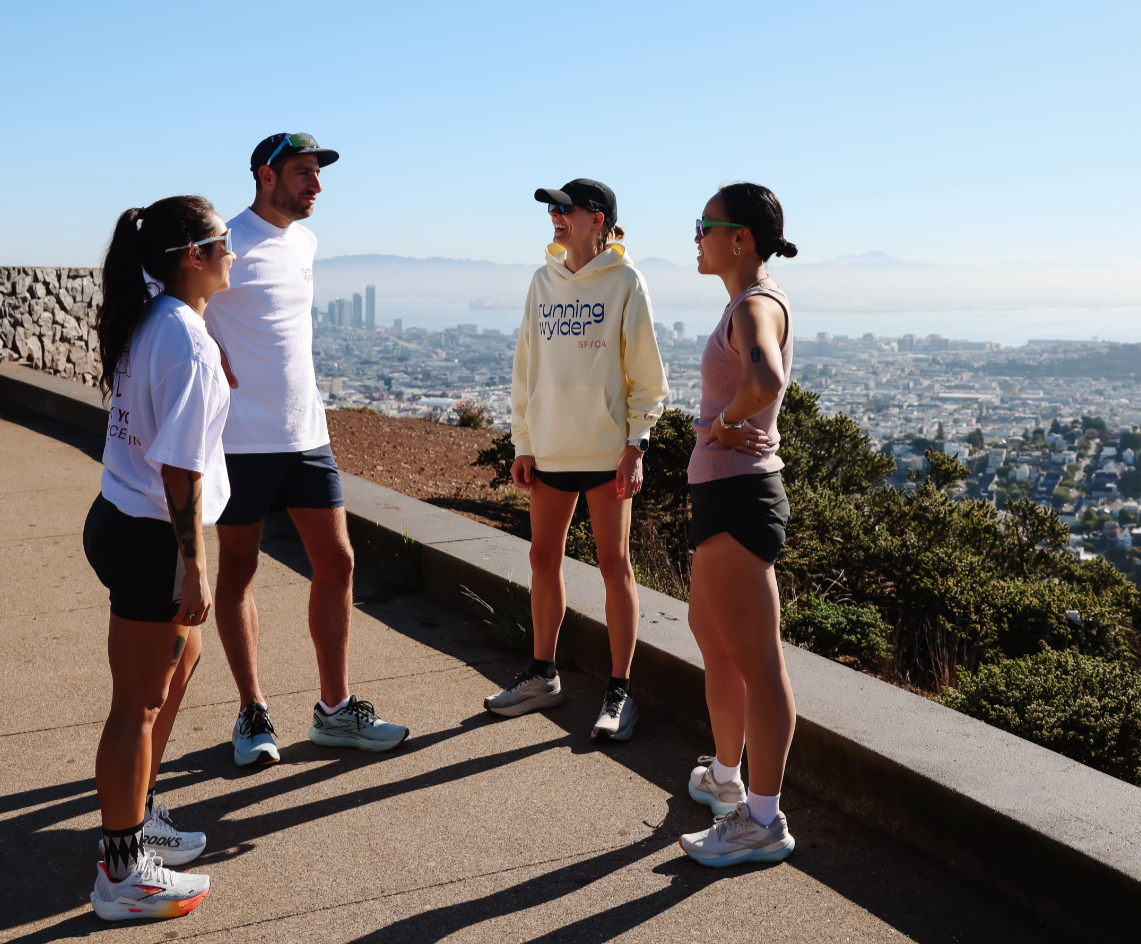 Group of four runners in Running Wylder gear chatting post-run at a San Francisco overlook with city and bay views