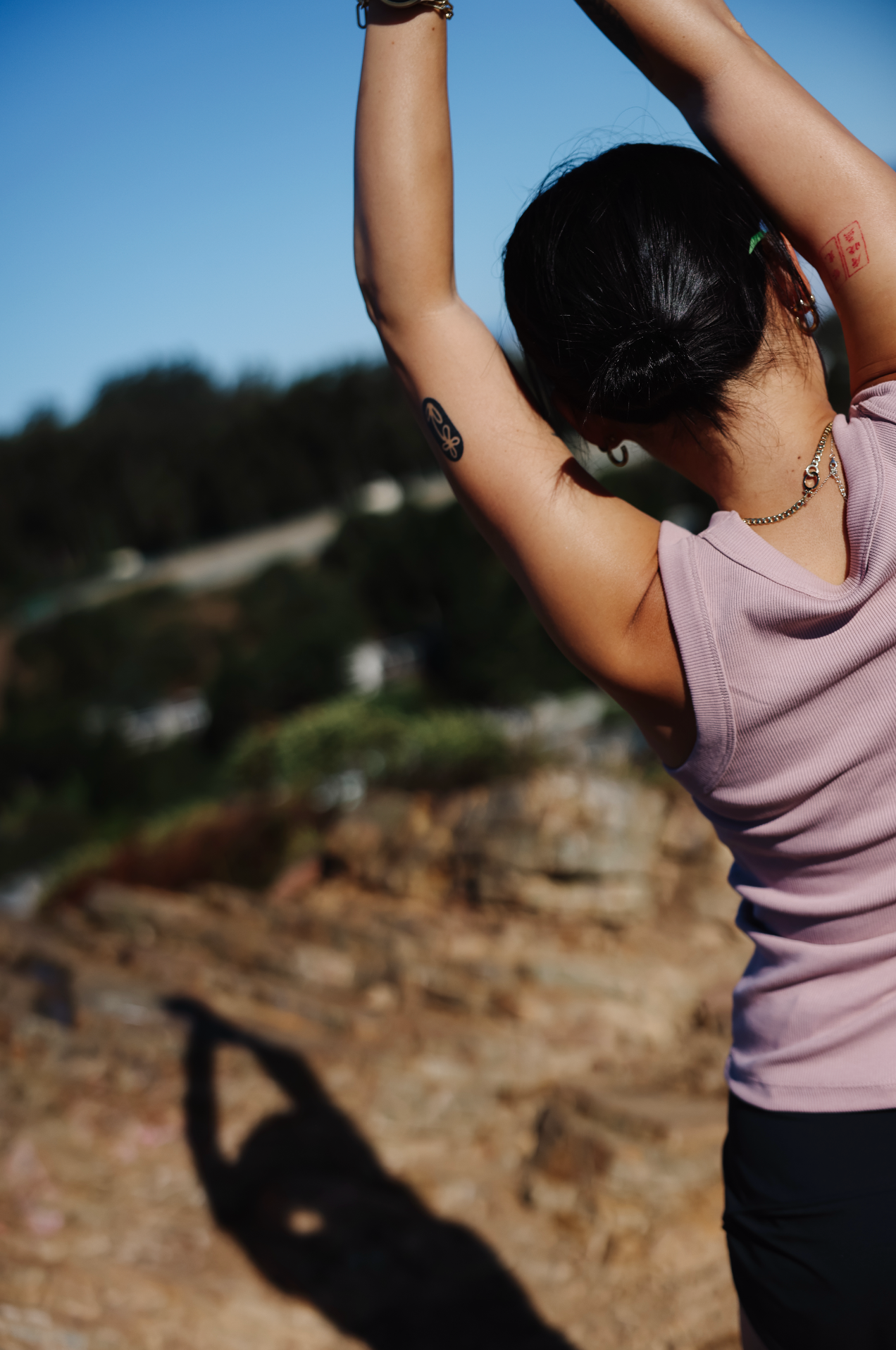 Runner stretching outdoors with arms overhead on a rocky trail in San Francisco, wearing a mauve tank top