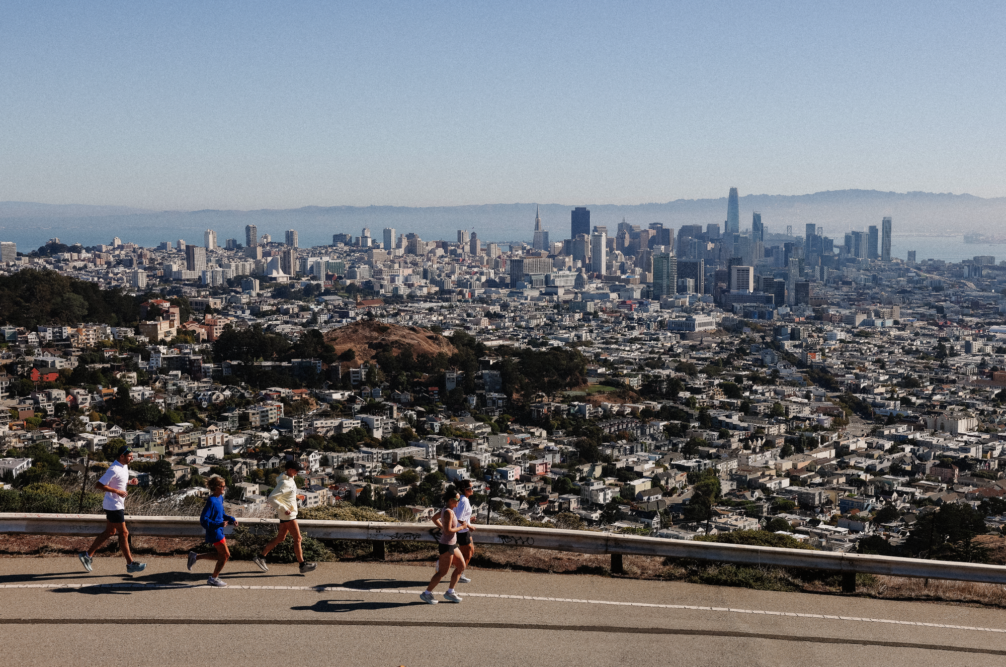 Group of runners in Running Wylder apparel jogging along Twin Peaks with a wide view of the San Francisco skyline