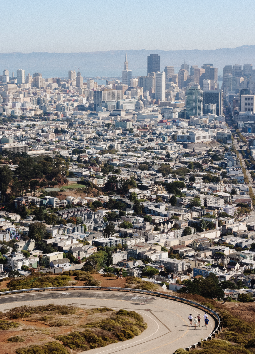 Aerial view of San Francisco skyline with group of runners on a winding trail at Twin Peaks in the foreground